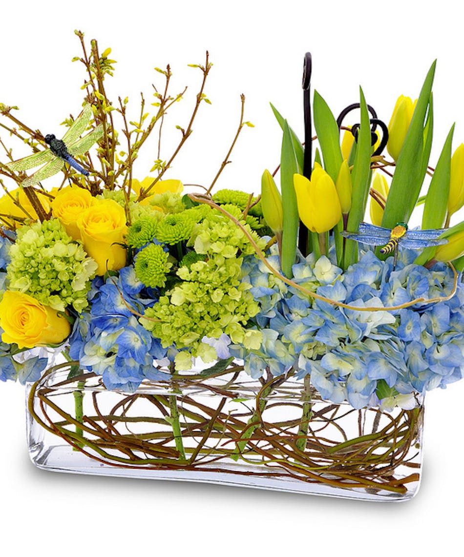 Blue hydrangea, yellow tulips and more in a long glass cube vase.